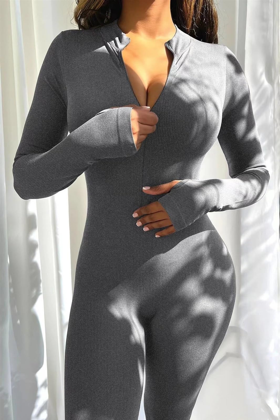 Person wearing a gray bodysuit against a white curtain background