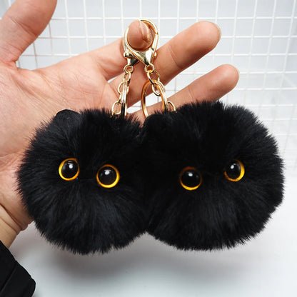Black fluffy keychain with gold chain held by a hand against a white background