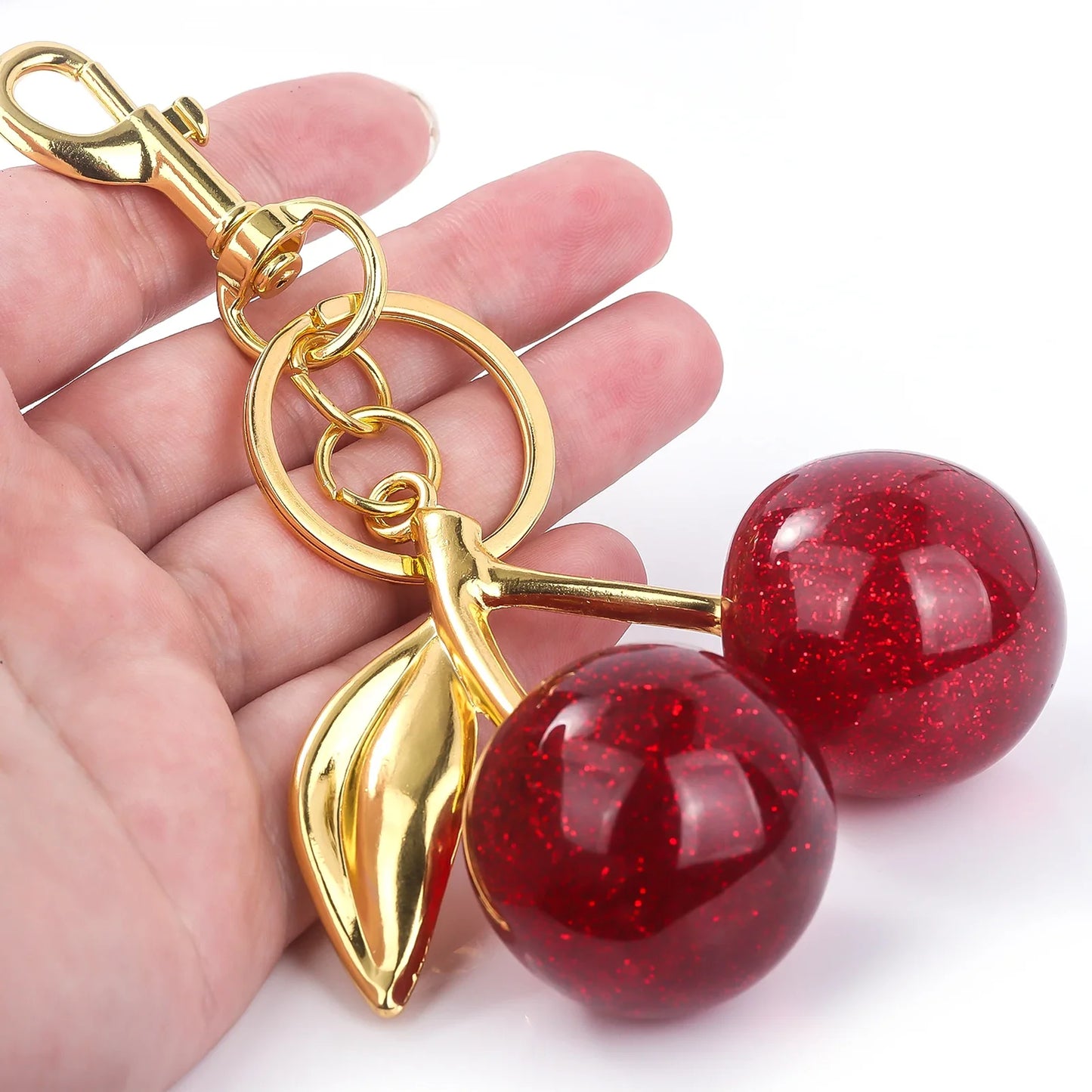 Gold keychain with red cherry-like charms held by a hand on a white background