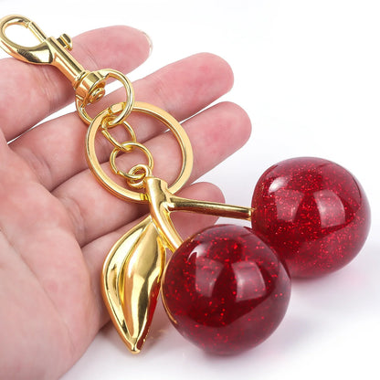 Gold keychain with red cherry-like charms held by a hand on a white background