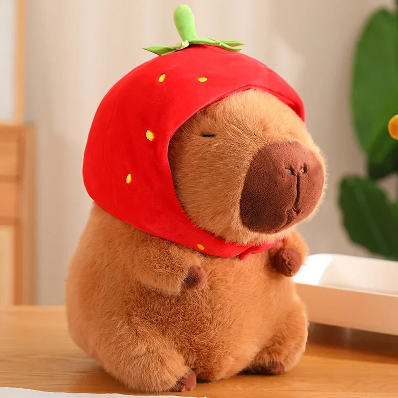 Plush toy resembling a bear wearing a red strawberry hat on a wooden surface.