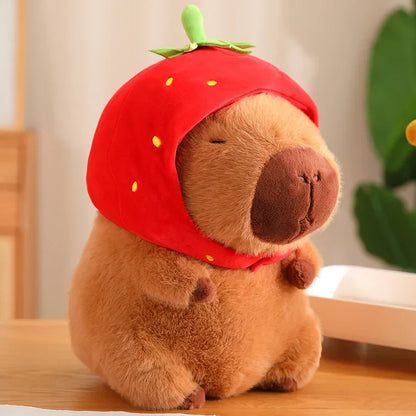 Plush toy resembling a bear wearing a red strawberry hat on a wooden surface.