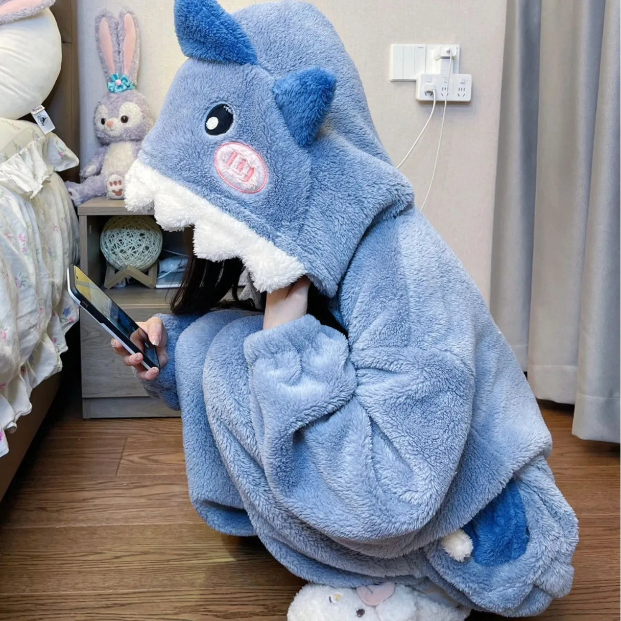 Person wrapped in a blue plush blanket with cartoon character design, sitting on the floor.