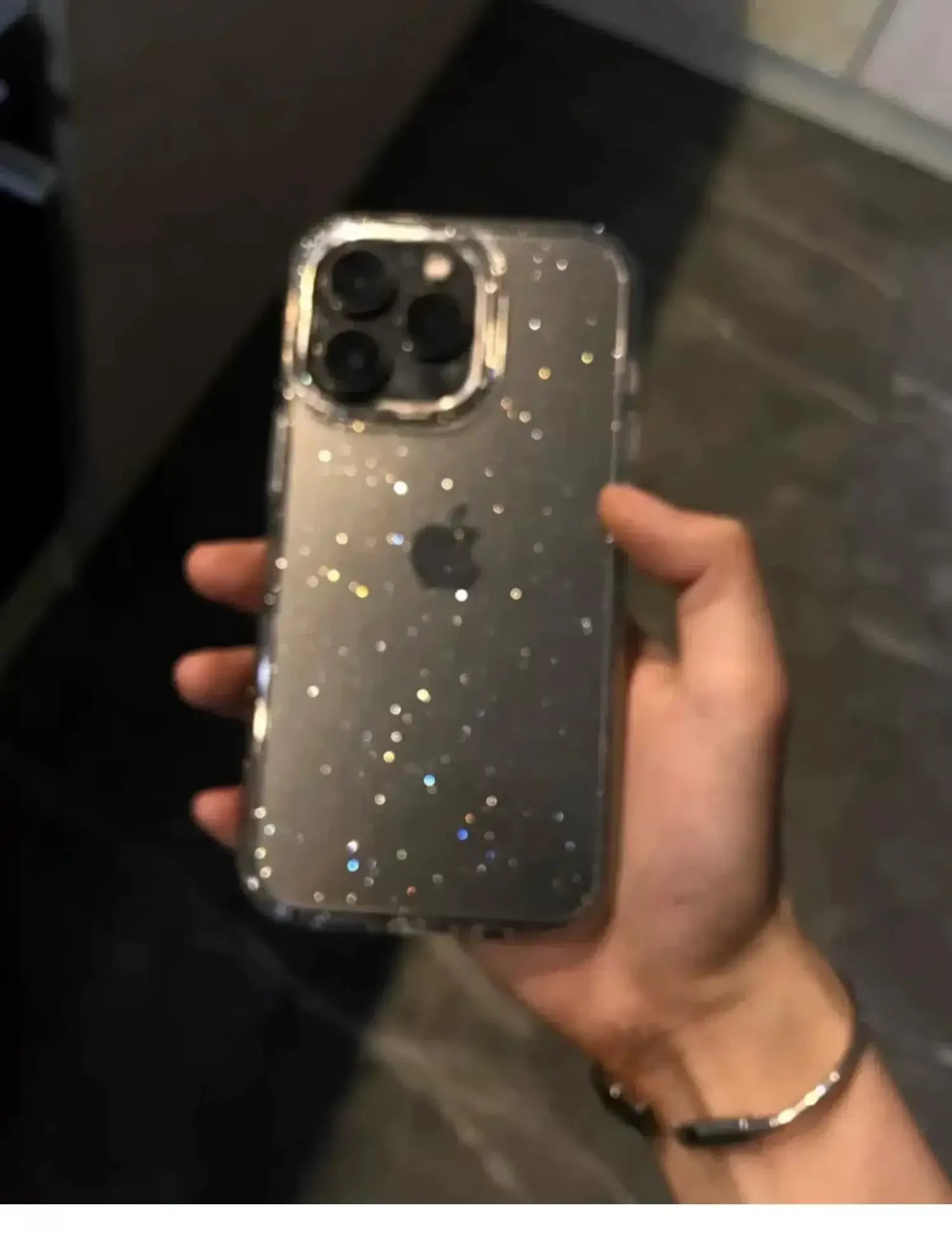 Hand holding a smartphone with a glittery case in an indoor setting