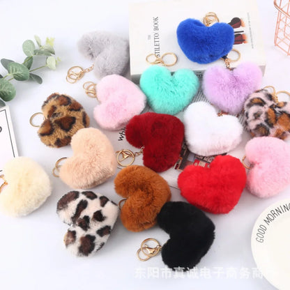 Collection of colorful heart-shaped keychains on a white surface with text and plants.