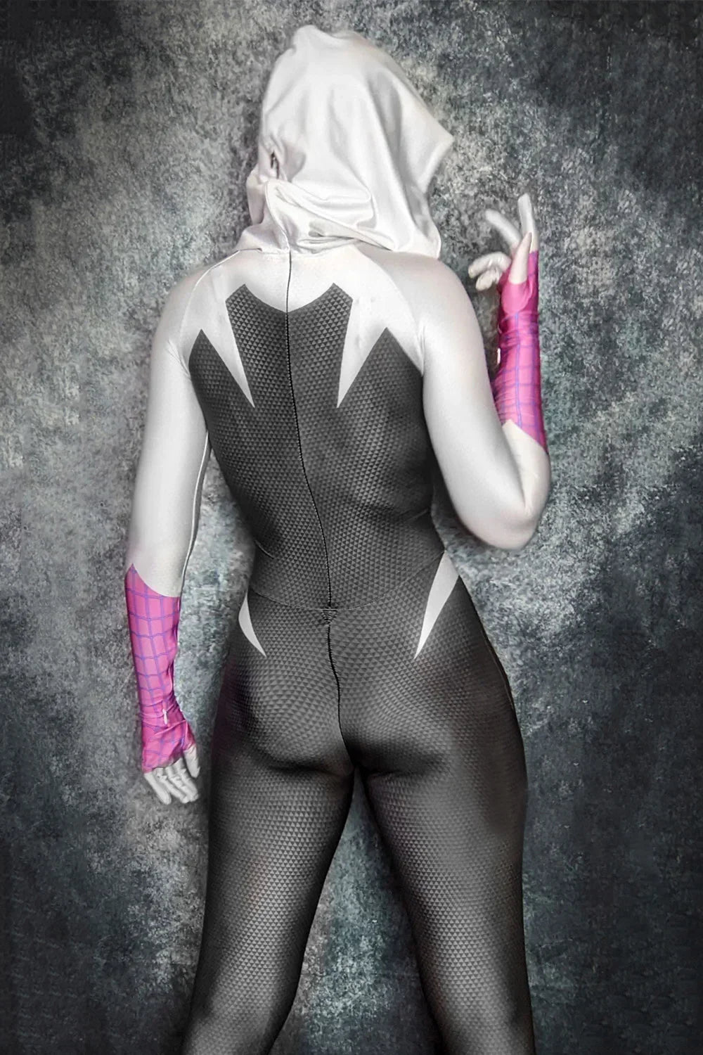 Person wearing a black bodysuit with white accents and pink gloves against a gray textured background