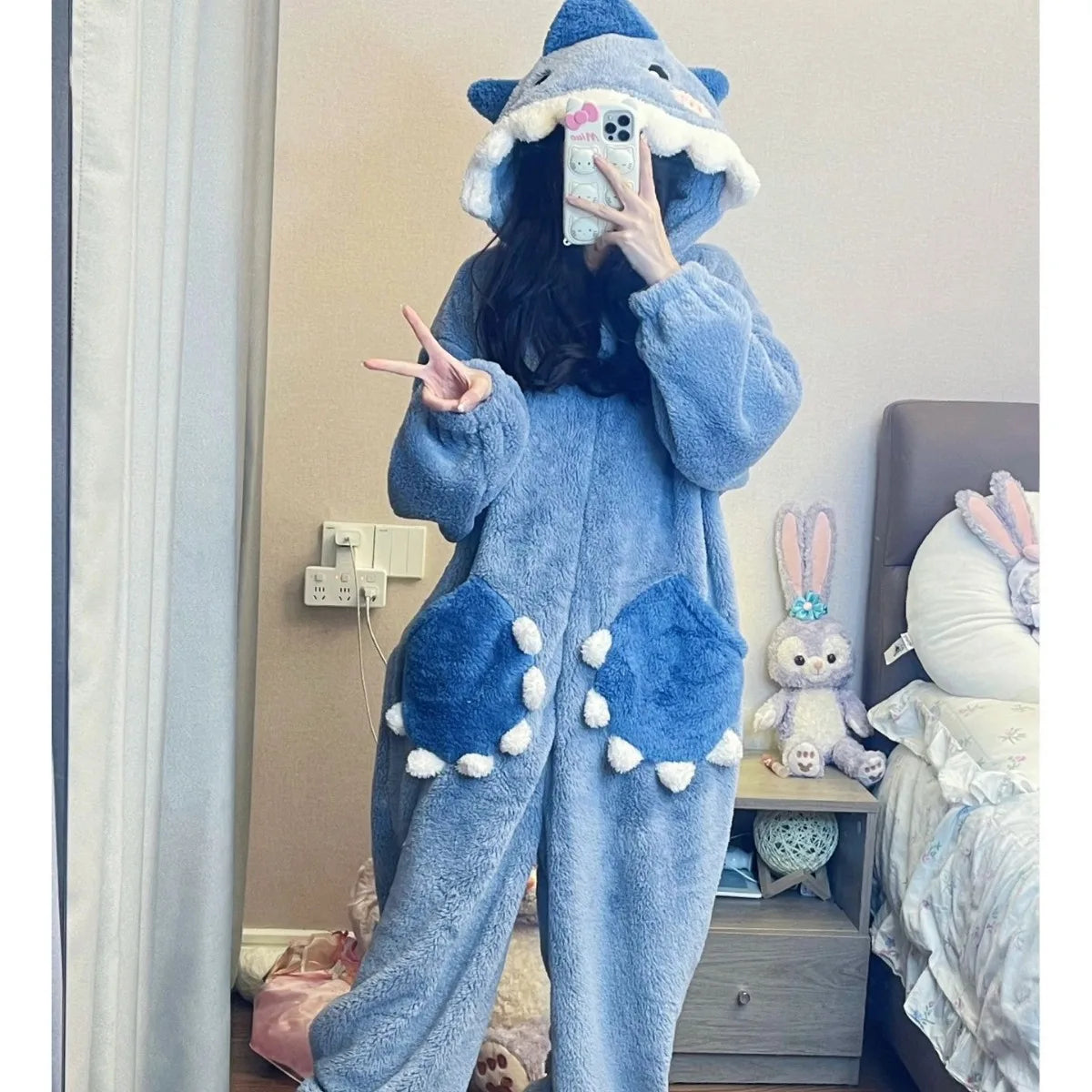 Person wearing a blue shark onesie in a bedroom setting.