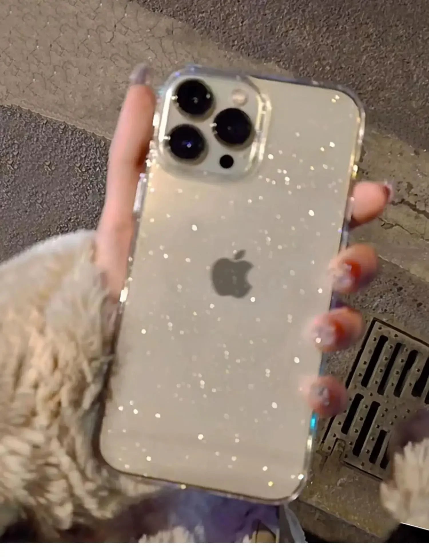 Phone with a glittery case held by a person against a textured wall.