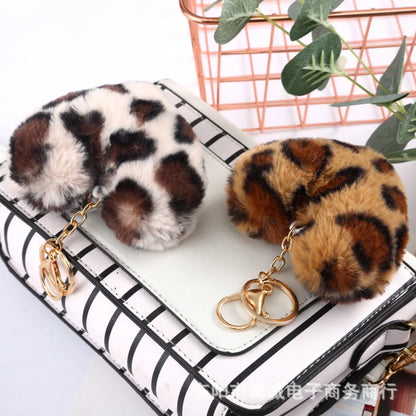 Leopard print keychains on a white surface with a plant in the background