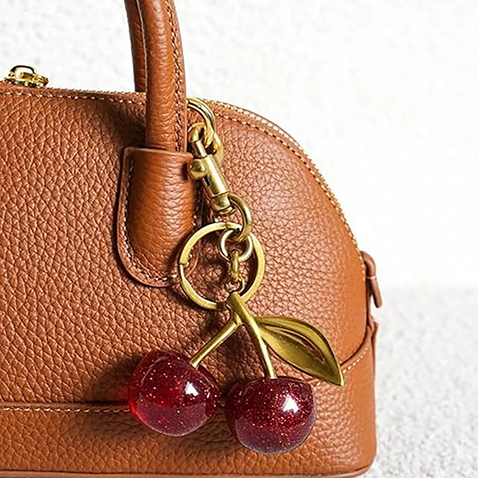 Brown leather handbag with a cherry keychain on a white background