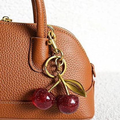 Brown leather handbag with a cherry keychain on a white background
