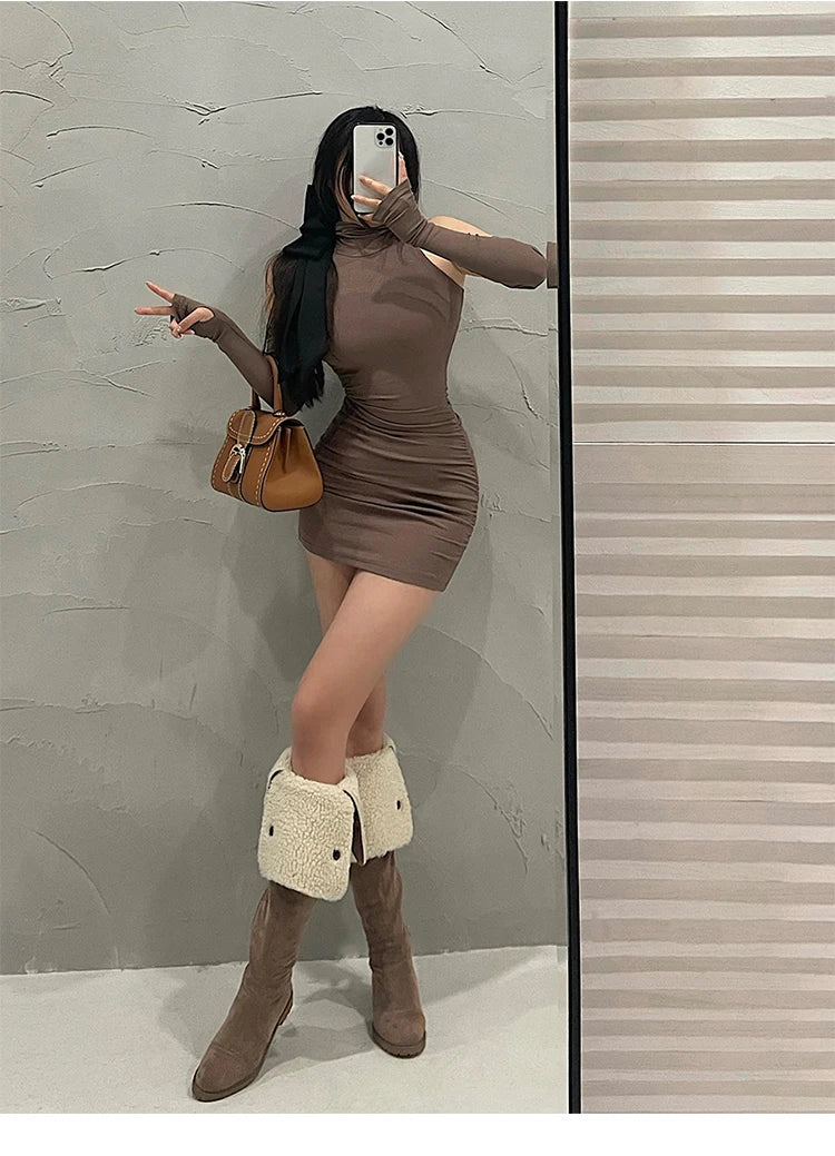 Person wearing a brown dress and knee-high boots, holding a brown handbag against a neutral wall.