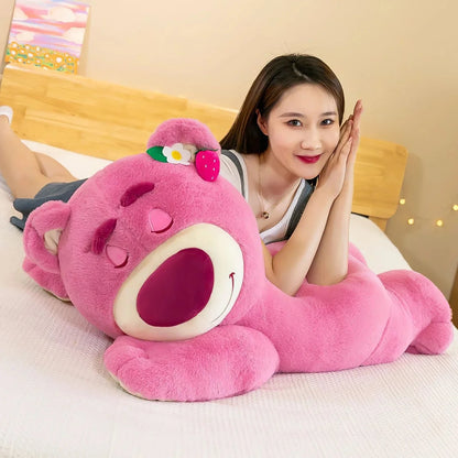 Woman sitting on a bed with a large pink plush toy resembling a cartoon character.