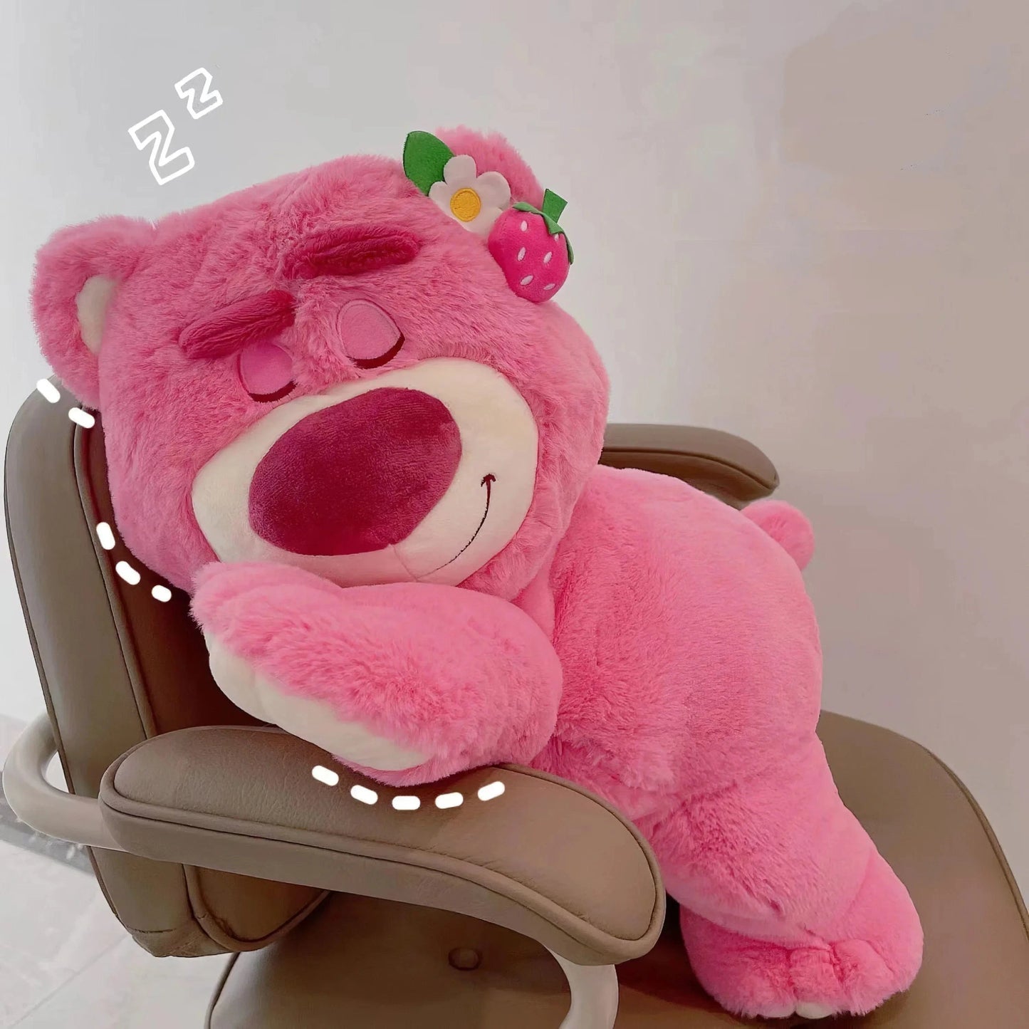 Pink teddy bear with a flower on its head sitting on a chair.