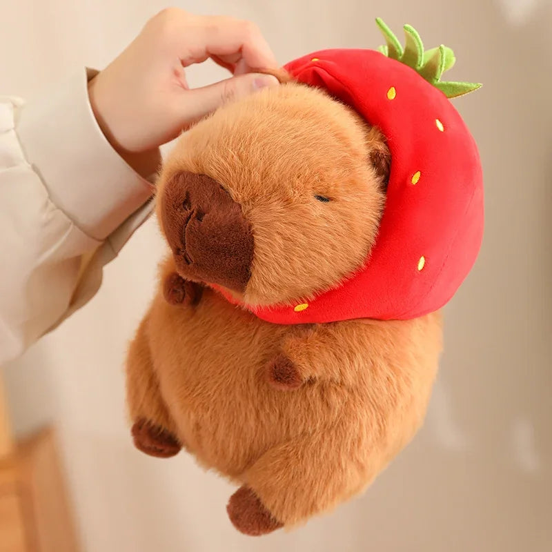 Plush toy bear wearing a strawberry hat held by a person against a neutral background