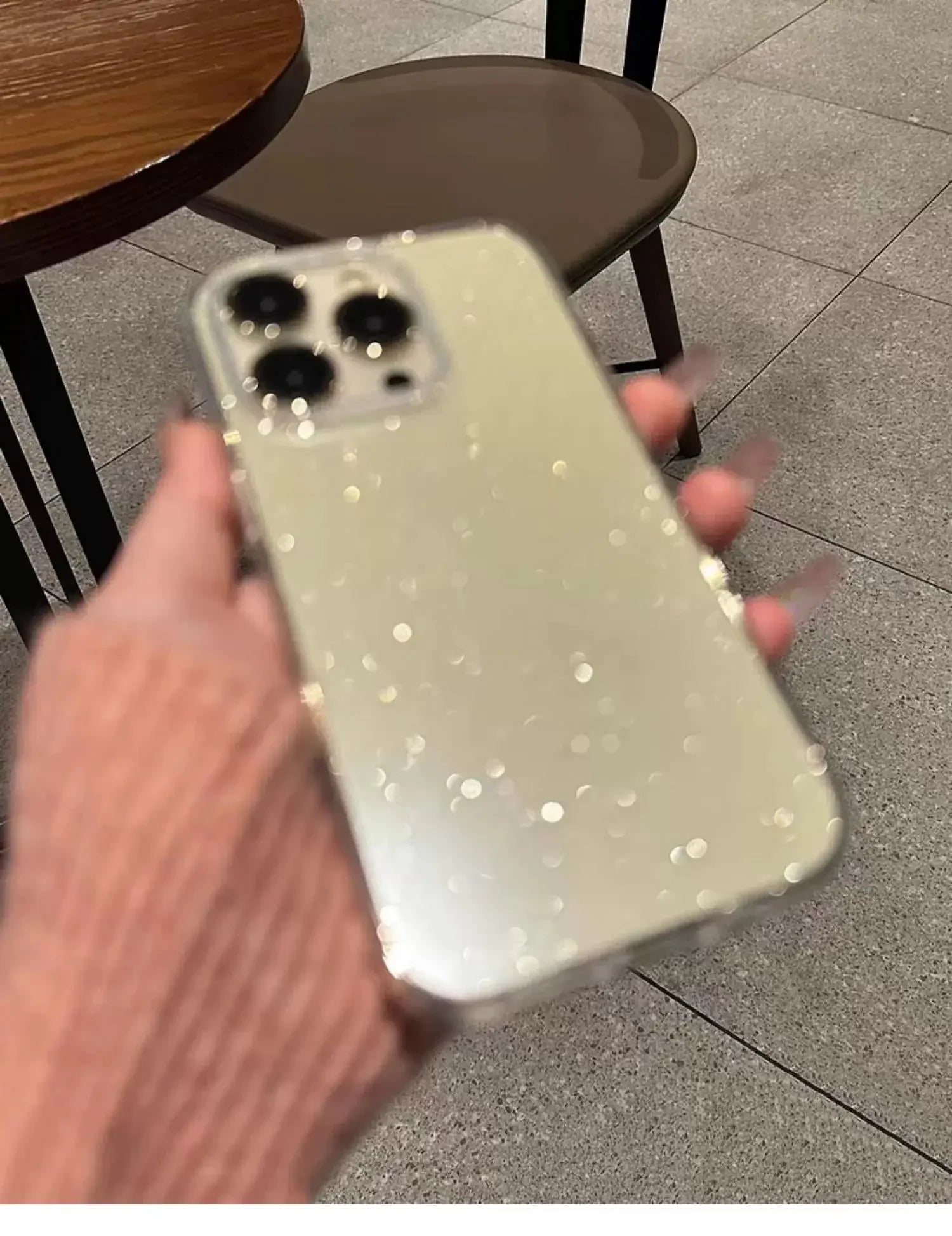 Phone case with glittery finish held by a hand on a tiled floor background