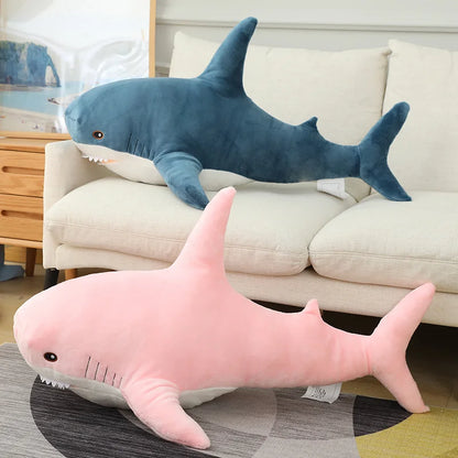 Two shark-shaped plush toys, one blue and one pink, on a couch and rug.