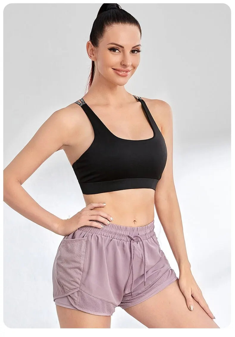 Woman wearing a black sports bra and purple shorts on a light gray background