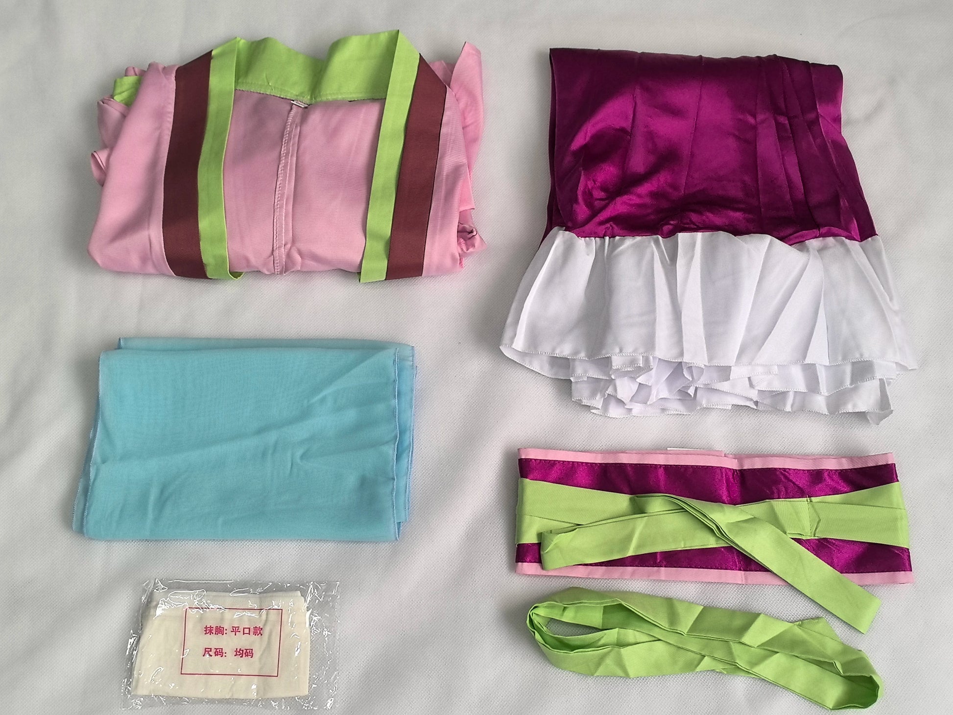 Collection of fabric pieces including a pink and green bag, purple and white top, blue fabric, and green belt on a light gray background.