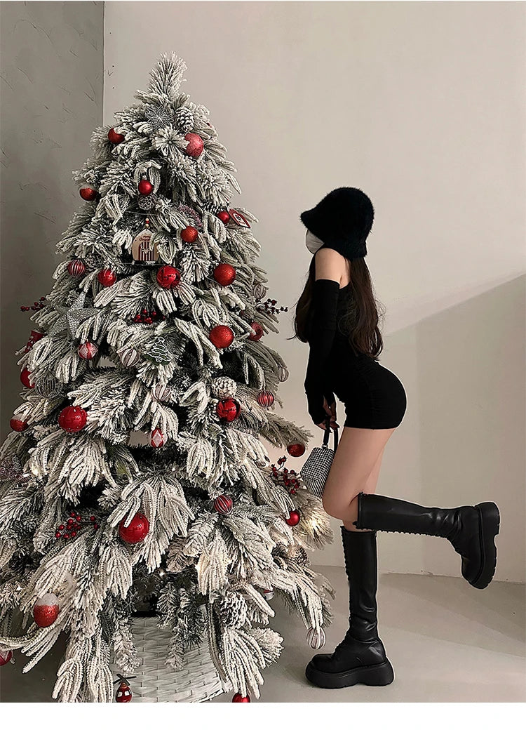 Person in black outfit standing next to a decorated Christmas tree with red ornaments.