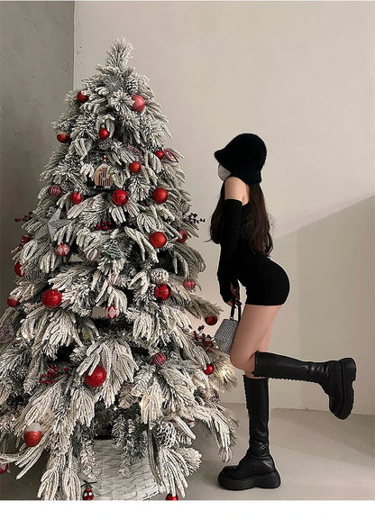 Person in black outfit standing next to a decorated Christmas tree with red ornaments.