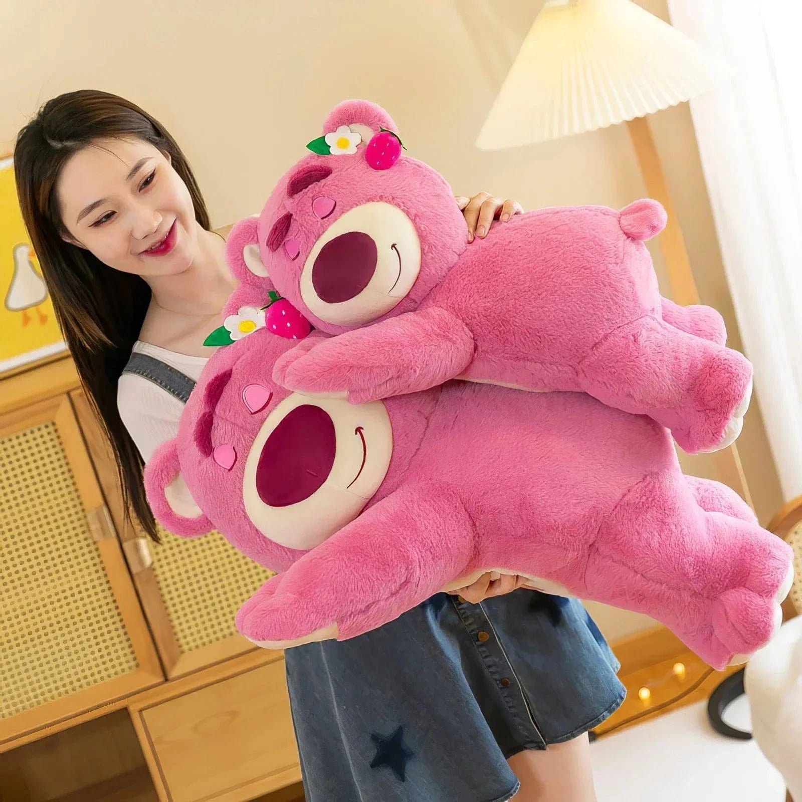 Person holding two large pink teddy bears in a room with wooden furniture.