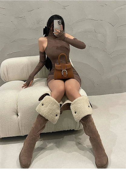 Person wearing a brown dress and knee-high boots sitting on a white chair with a gray textured wall background.
