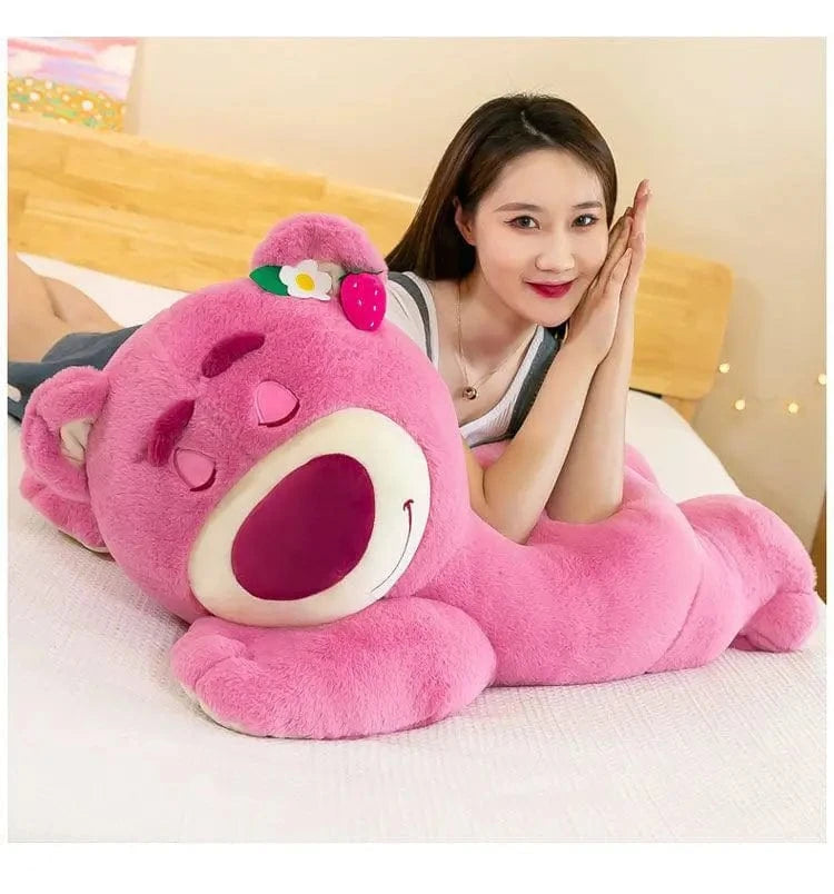 Woman lying on a bed with a large pink plush toy resembling a cartoon character.