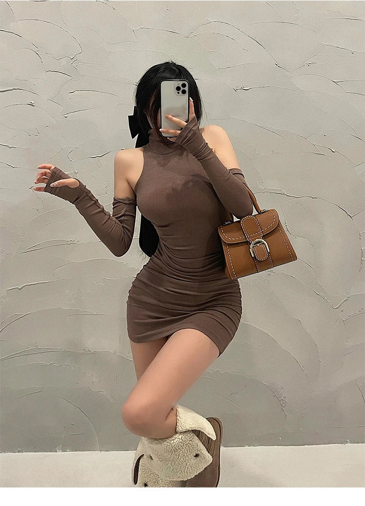 Person wearing a brown dress and holding a brown handbag against a gray wall.