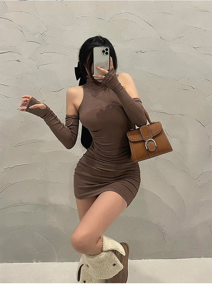 Person wearing a brown dress and holding a brown handbag against a gray wall.