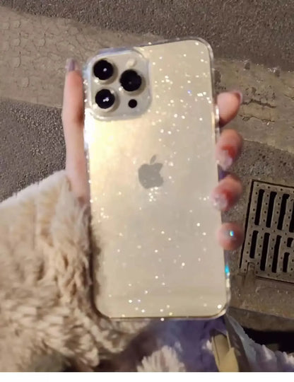 Phone with a glittery case held by a person, on a textured surface.