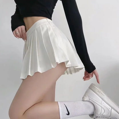 Person wearing a white pleated skirt, black long-sleeve top, and white sneakers on a plain background