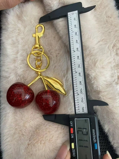 Gold cherry-shaped keychain with a digital caliper measuring its length on a fur surface.