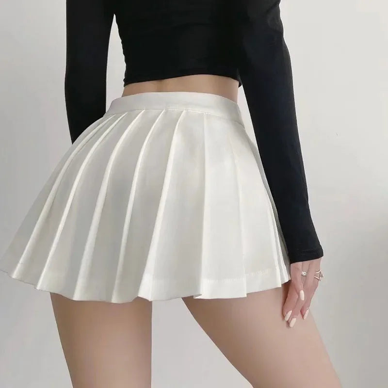 Person wearing a white pleated skirt and black long-sleeve top on a plain background
