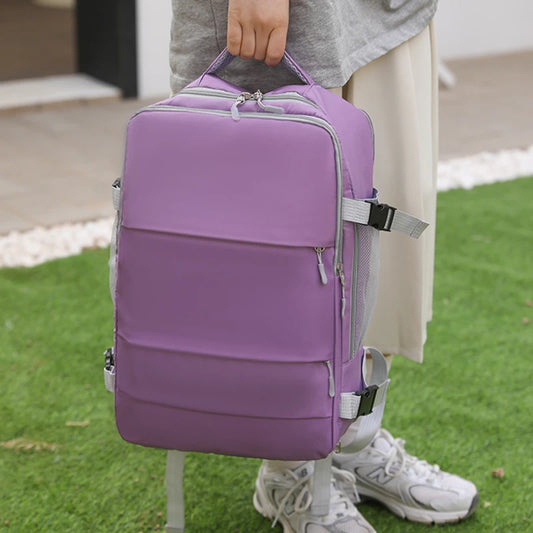Purple backpack with gray straps held by a person on grass