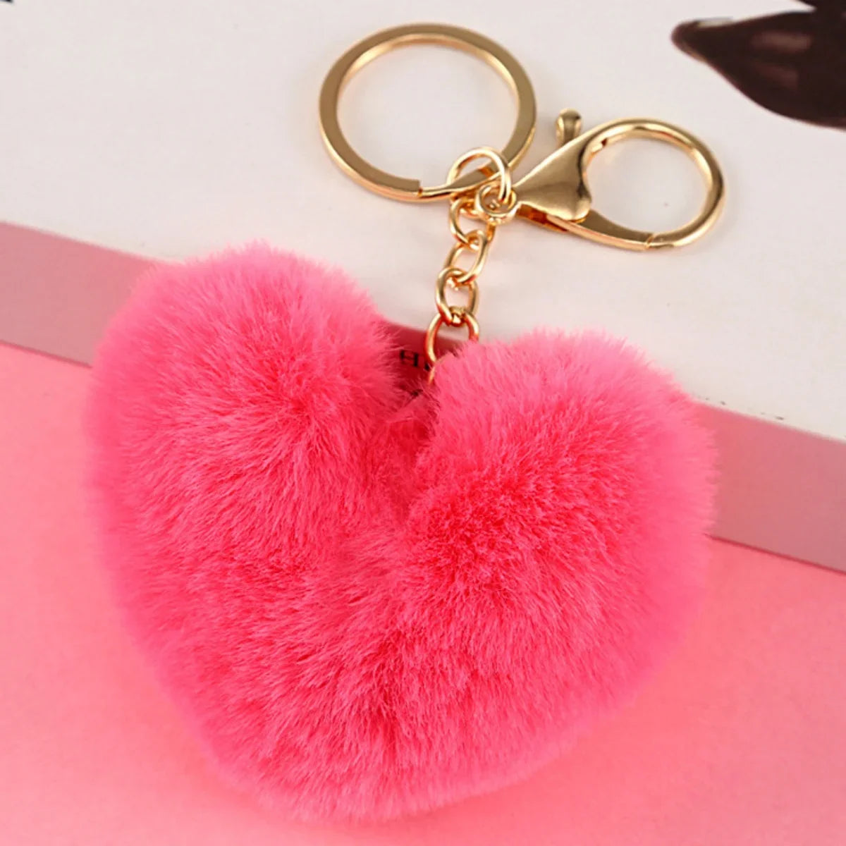 Pink heart-shaped fluffy keychain with a gold clasp on a pink background
