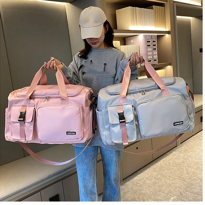 Person holding two duffel bags, one pink and one gray, in a room.
