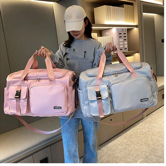 Person holding two duffel bags, one pink and one gray, in a room.