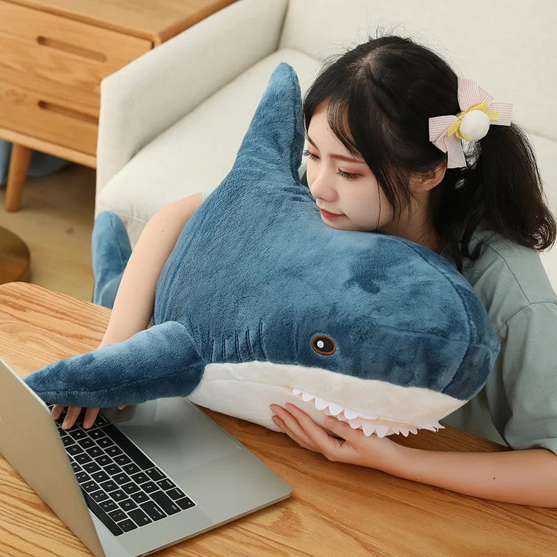 Person using a laptop with a large blue shark-shaped pillow on their lap