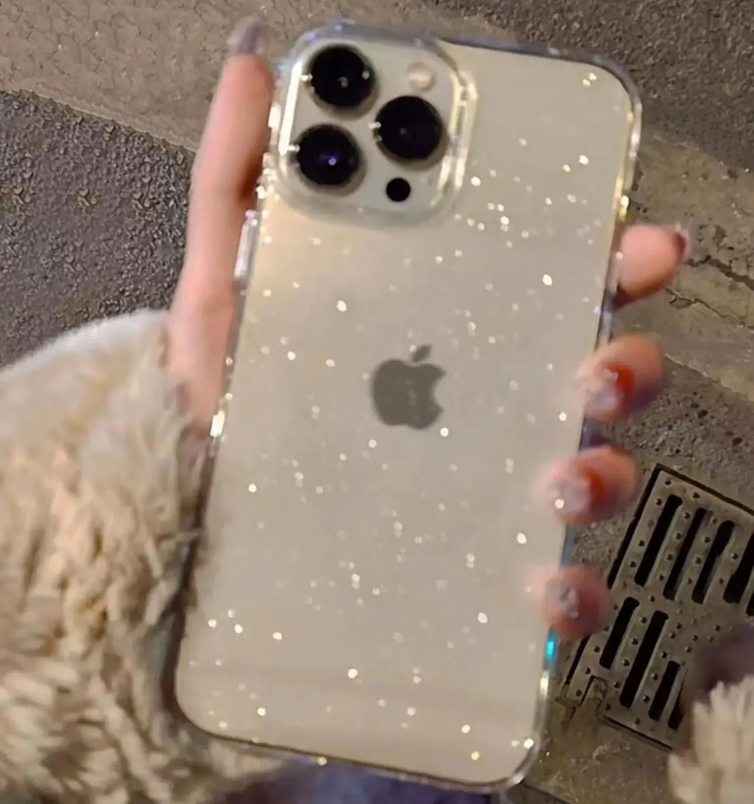 Phone with glittery case held by a person, against a textured wall background