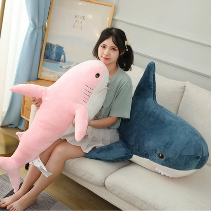 Woman holding a pink shark plush toy next to a blue shark plush toy on a couch.