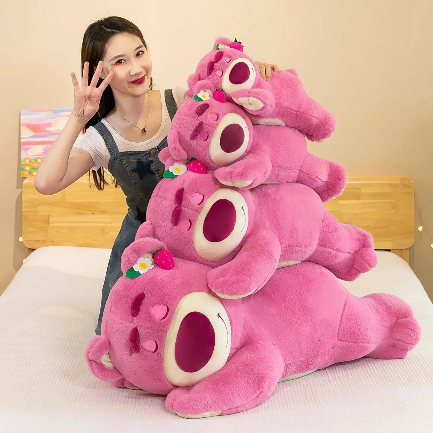 Stack of pink plush toys resembling cartoon characters on a bed with a person in the background.