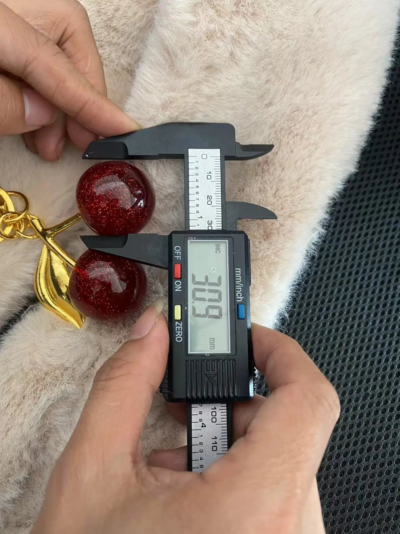 Digital caliper measuring a red cherry-like object against a textured background