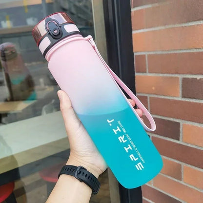 Gradient water bottle with pink and blue design held by a person, against a brick wall.