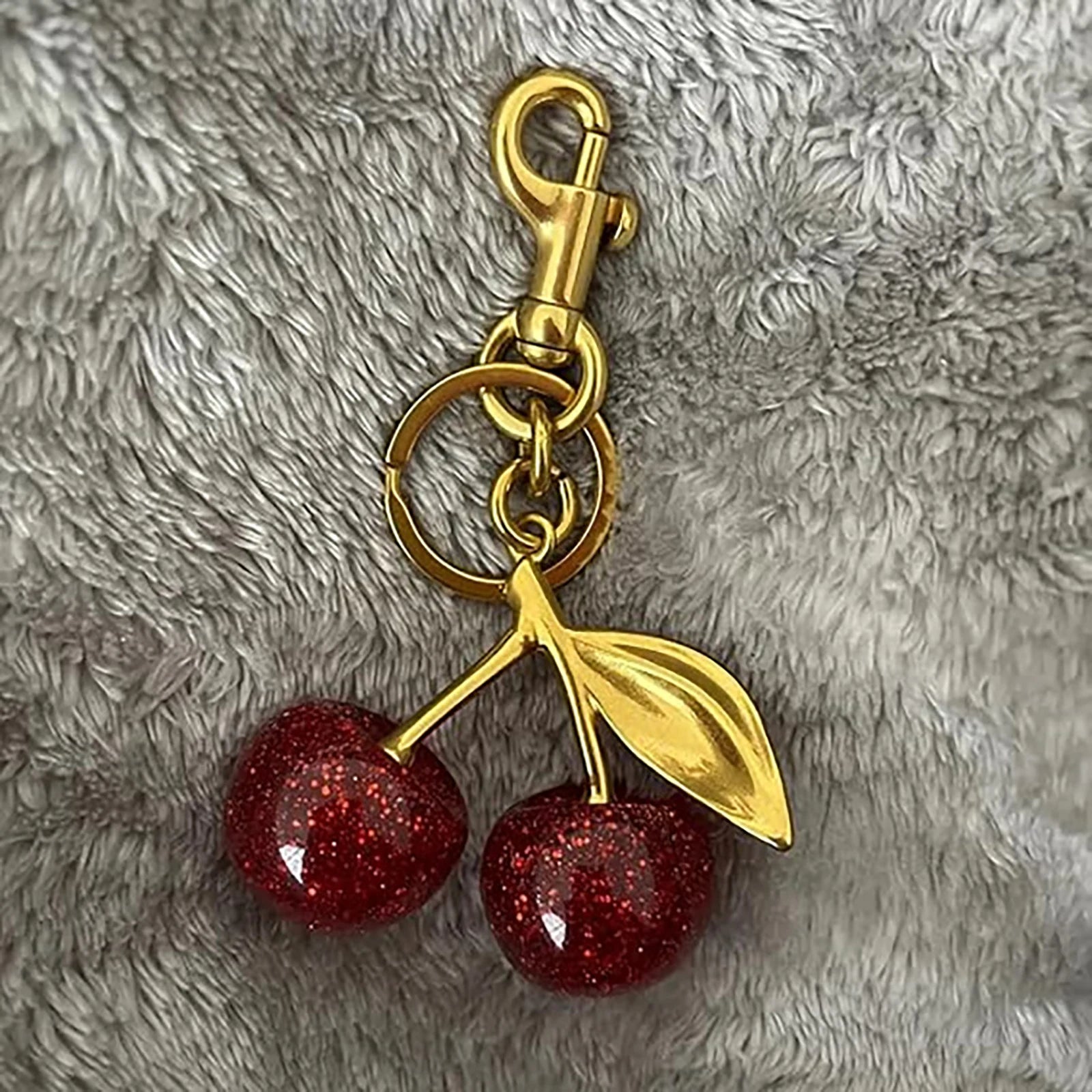 Keychain with red cherries and gold stem on a textured gray background